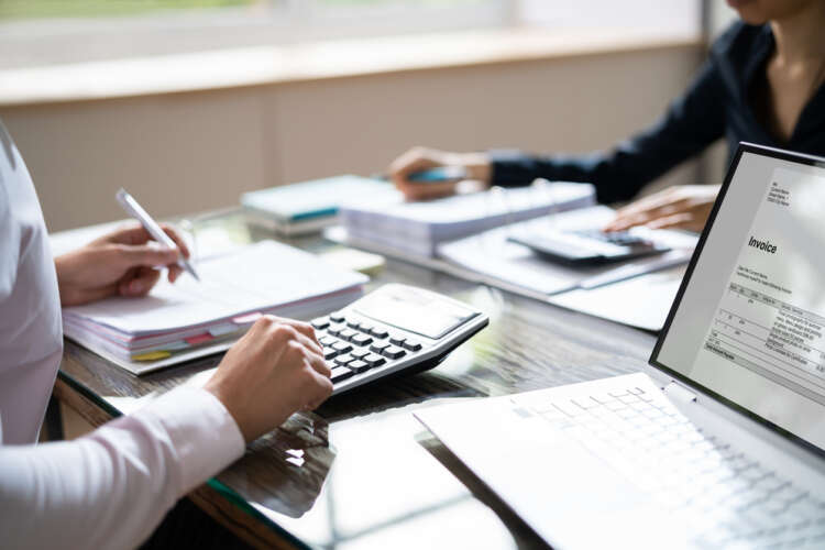 Elevated View Of Two Businesspeople Calculating Invoice With Calculator At Workplace